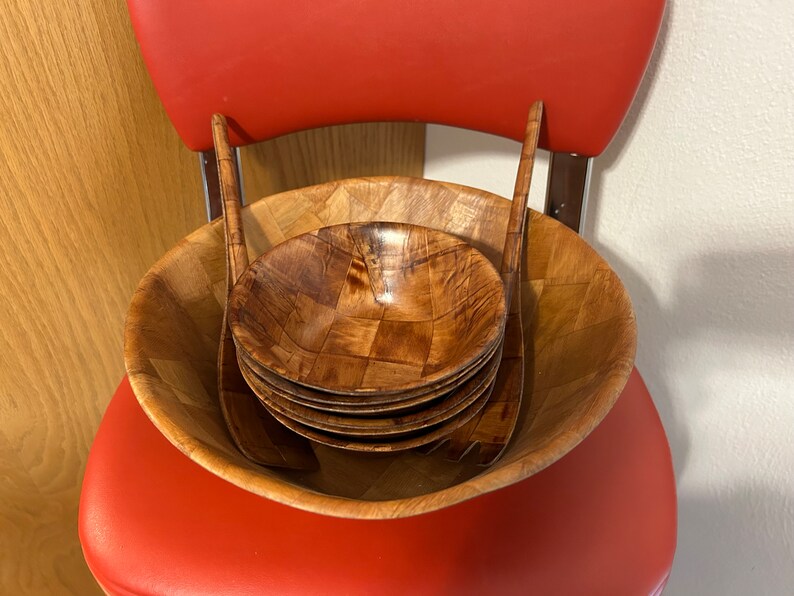Pu&ograve; includere: Un set di insalatiere e utensili da servizio in legno. Le insalatiere sono impilate all'interno di una ciotola pi&ugrave; grande, e gli utensili sono posizionati sopra le insalatiere. Le insalatiere sono realizzate in legno marrone chiaro e hanno un motivo intrecciato.