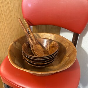 Pu&ograve; includere: Un set di insalatiere e cucchiai da portata in legno. Le insalatiere sono impilate e i cucchiai sono posizionati sopra le insalatiere. Le insalatiere sono in legno marrone chiaro e hanno un motivo intrecciato. I cucchiai sono anch'essi in legno marrone chiaro e hanno una finitura liscia.