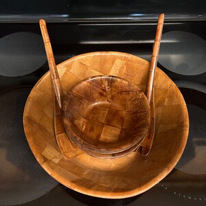 Pu&ograve; includere: Un set di tre insalatiere in legno con un motivo intrecciato. Le insalatiere sono annidate l'una dentro l'altra e hanno due utensili da portata in legno.