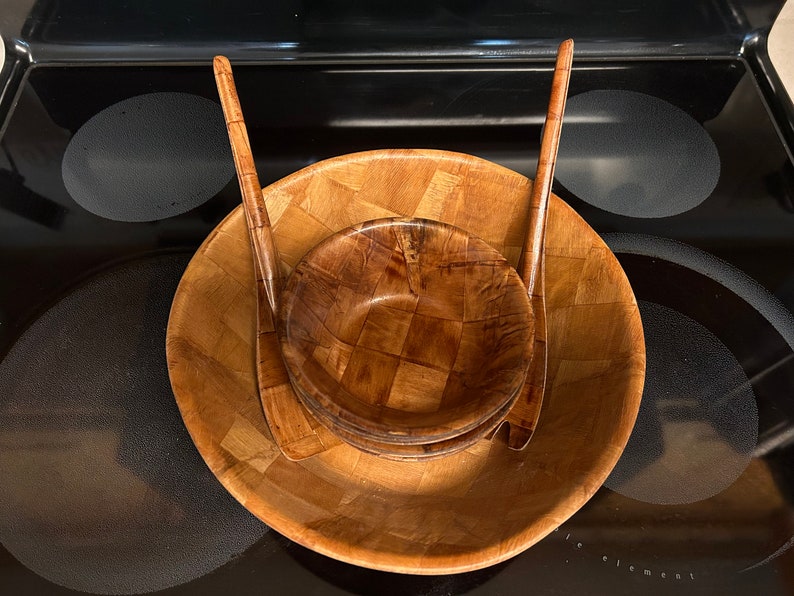 Pu&ograve; includere: Un set di tre insalatiere in legno con un motivo intrecciato. Le insalatiere sono annidate l'una dentro l'altra e hanno due utensili da portata in legno.