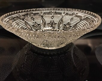 May include: A clear glass bowl with a decorative, embossed pattern of leaves and swirls. The bowl is on a black surface.