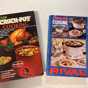 May include: Two cookbooks with blue and black covers. The book on the left is titled "Crock-Pot Cooking" and features a roasted chicken and a slow cooker. The book on the right is titled "Crock-Pot Slow Cooker Cuisine" and features a variety of slow cooker dishes.