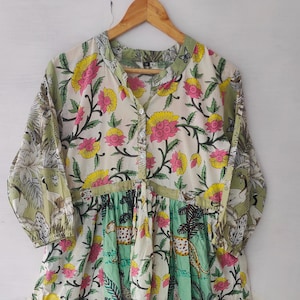 Könnte beinhalten: Ein langes Kleid mit floralem Muster, Stehkragen und Knopfleiste. Das Kleid hat einen weißen Hintergrund mit rosa und gelben Blumen sowie grüne und türkisfarbene Bahnen mit Tier- und Dschungelmotiven.