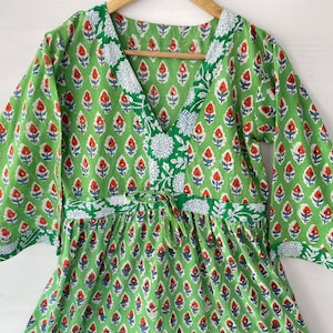 May include: A green cotton dress with a V-neck and three-quarter sleeves. The dress features a repeating floral pattern in red, white, and blue on a green background. The neckline and waist have white floral accents.