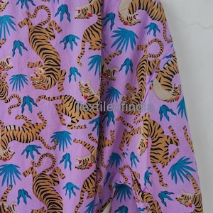 May include: A lilac-colored robe with a repeating pattern of tigers in shades of brown and black, along with teal-colored leaf shapes. The robe has white trim and a matching belt.