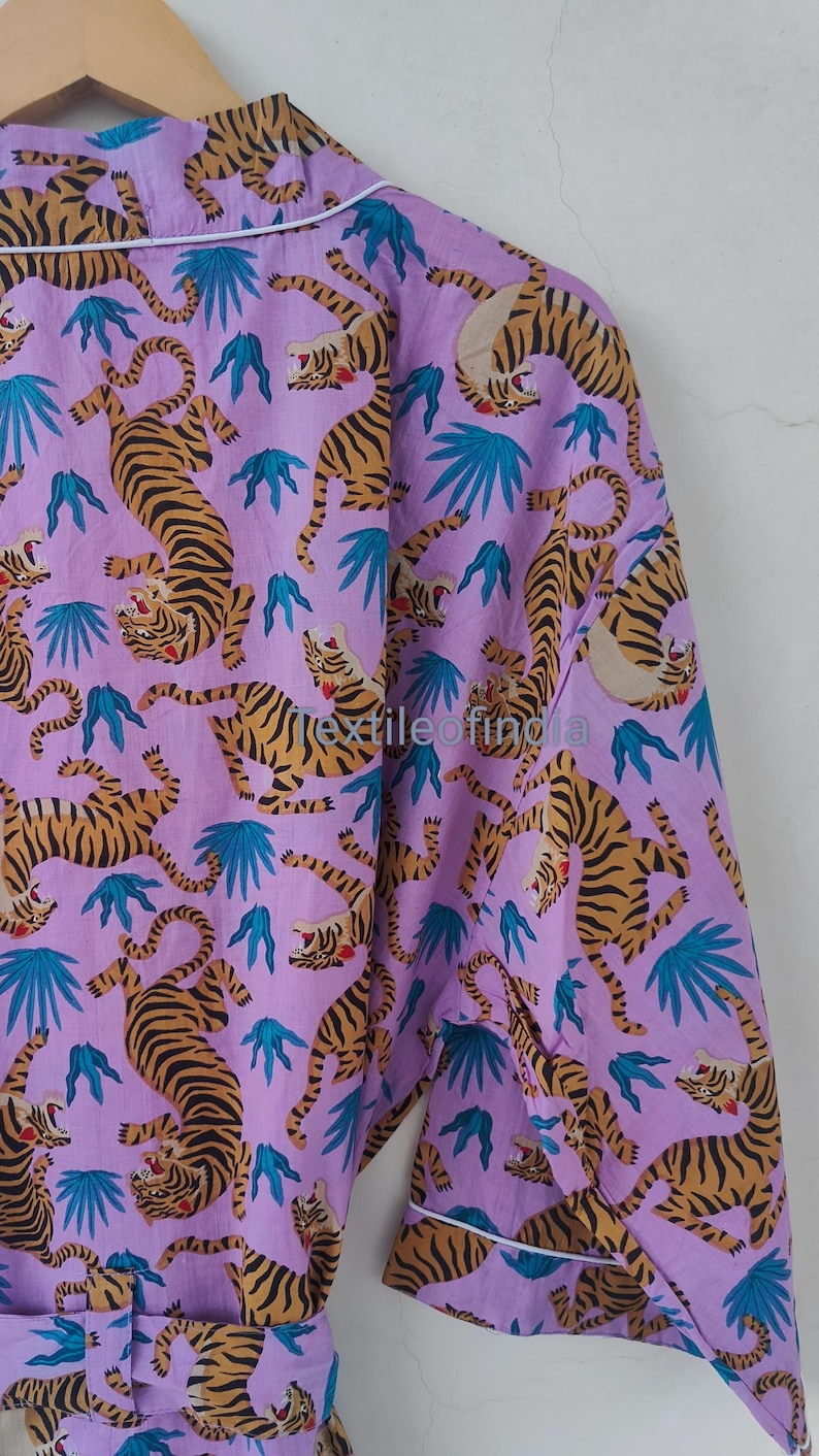 May include: A lilac-colored robe with a repeating pattern of tigers in shades of brown and black, along with teal-colored leaf shapes. The robe has white trim and a matching belt.