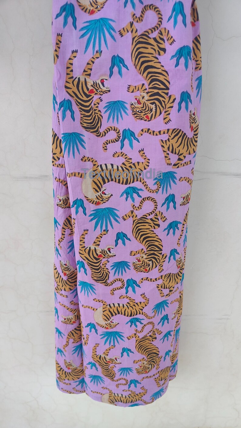 May include: A lavender fabric with a repeating pattern of tigers in shades of orange and black, interspersed with teal-colored leaf shapes. The tigers are depicted in various poses, creating a dynamic and eye-catching design.