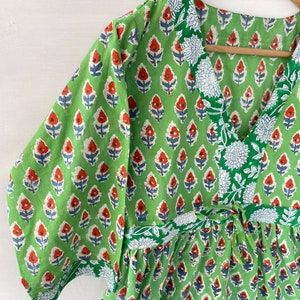 May include: A green, short-sleeved dress with a V-neck and a floral pattern. The pattern features red and blue flowers on a green background. The dress has a tie at the waist and white floral trim.