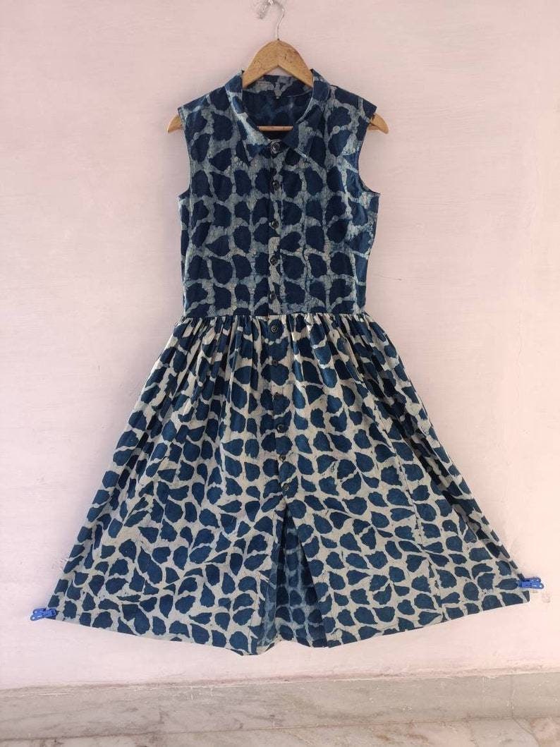 Puede incluir: Un vestido azul y blanco sin mangas con cierre de botones en la parte delantera y falda fruncida. El vestido tiene un estampado de hojas.
