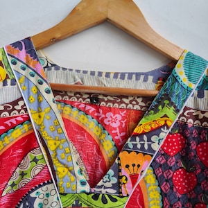 Peut inclure: Un haut &agrave; col en V color&eacute; et multi-motifs avec une bordure blanche. Le tissu pr&eacute;sente une vari&eacute;t&eacute; de motifs g&eacute;om&eacute;triques et floraux dans des tons de rouge, bleu, vert, jaune et marron.