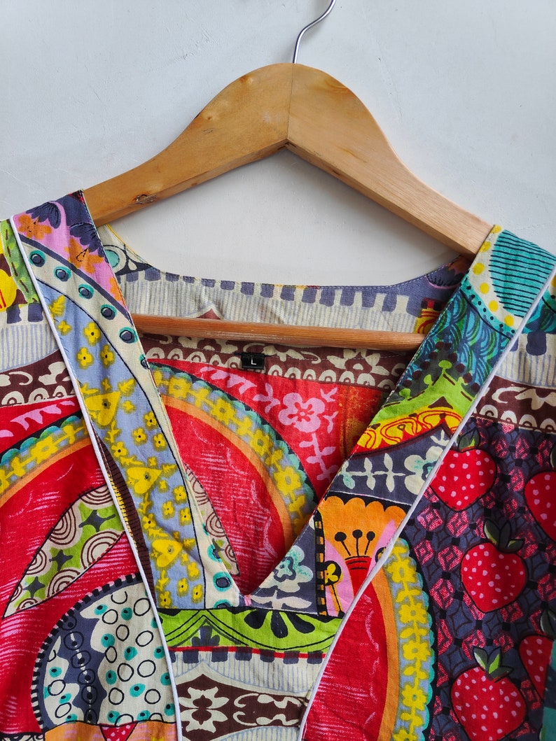 Peut inclure: Un haut &agrave; col en V color&eacute; et multi-motifs avec une bordure blanche. Le tissu pr&eacute;sente une vari&eacute;t&eacute; de motifs g&eacute;om&eacute;triques et floraux dans des tons de rouge, bleu, vert, jaune et marron.