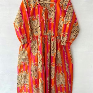 Può includere: Un lungo vestito a righe arancioni e rosa con stampa di tigre. Il vestito ha un nodo sul collo e maniche 3/4.