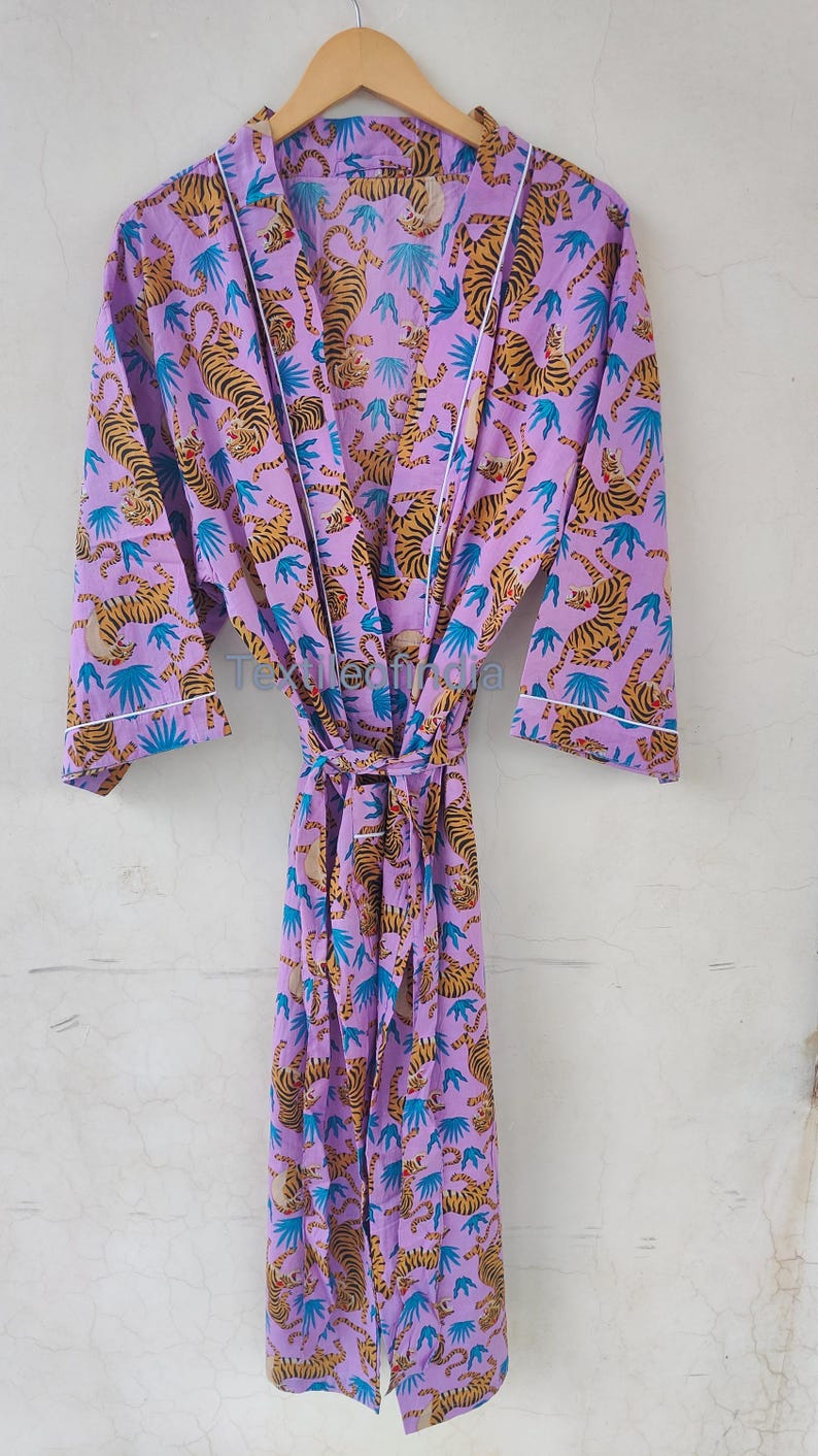 May include: A lilac-colored robe with a repeating pattern of tigers and blue leaf shapes. The robe has a white trim and a matching tie belt. The text "Textileofindia" is visible on the robe.