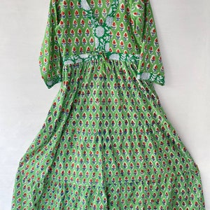 May include: A green, long-sleeved dress with a V-neck and a floral pattern. The dress features a repeating pattern of red and blue floral motifs on a green background. White floral accents are present on the neckline and waist.