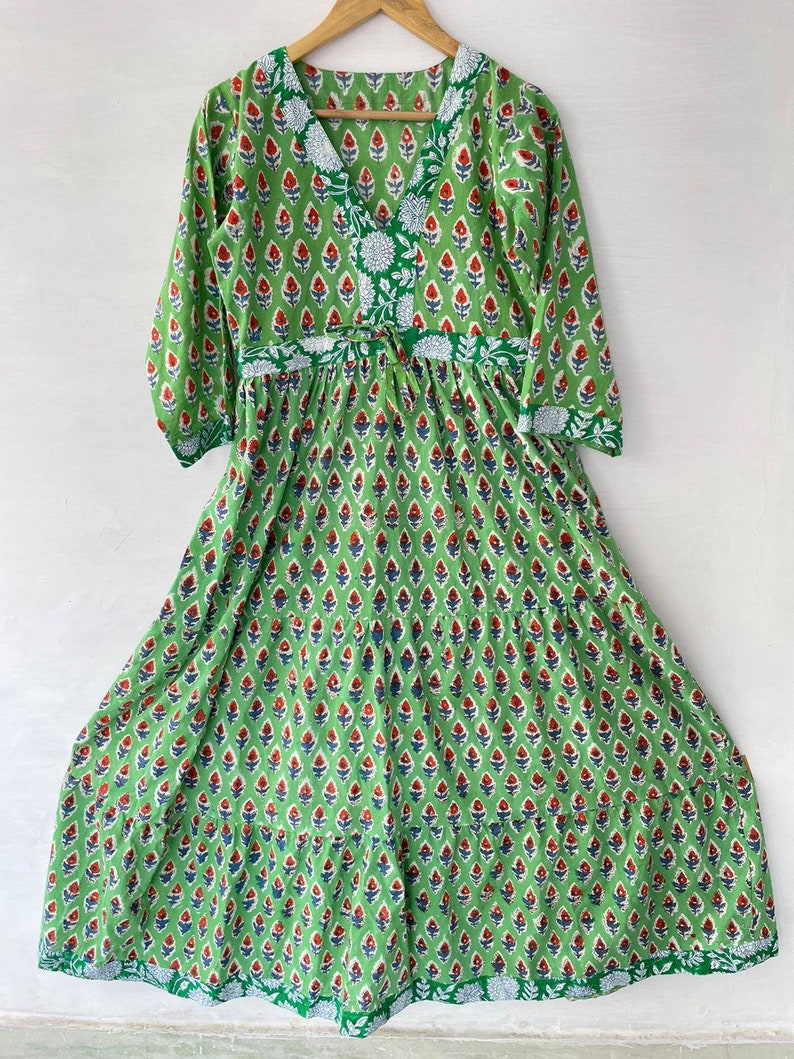 May include: A green, long-sleeved dress with a V-neck and a floral pattern. The dress features a repeating pattern of red and blue floral motifs on a green background. White floral accents are present on the neckline and waist.