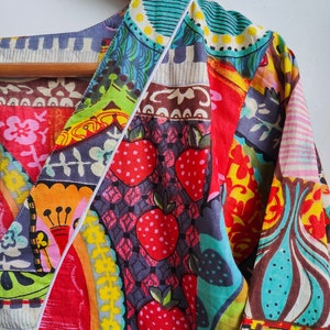 Peut inclure: Une chemise color&eacute;e &agrave; motifs multiples avec un col en V et des manches longues. Le tissu pr&eacute;sente un design patchwork avec diff&eacute;rentes formes g&eacute;om&eacute;triques, des motifs floraux et des fraises.