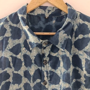 Puede incluir: Una camisa azul y blanca con estampado y cierre de botones. La camisa tiene cuello y est&aacute; colgada de una percha de madera. La etiqueta de talla dice "M".