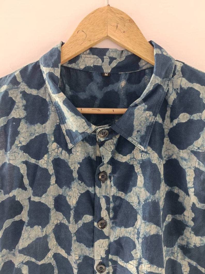 Puede incluir: Una camisa azul y blanca con estampado y cierre de botones. La camisa tiene cuello y est&aacute; colgada de una percha de madera. La etiqueta de talla dice "M".