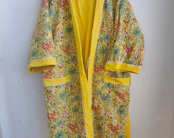 Puede incluir: Una bata acolchada amarilla con estampado floral. La bata tiene un cinturón de atar y dos bolsillos.