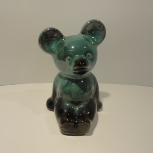 May include: A ceramic bear figurine with a teal glaze and black accents. The bear is sitting with its legs crossed and has a small, black nose.