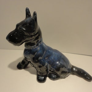 Può includere: Una statuetta in ceramica nera e blu di un terrier scozzese seduto con la coda arrotolata dietro.