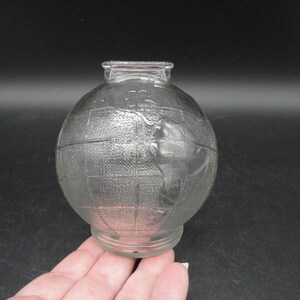 Puede incluir: Una alcancía de vidrio transparente en forma de globo terráqueo con una superficie texturizada. El globo presenta un contorno en relieve de los continentes.