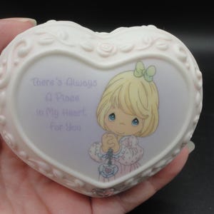 Puede incluir: Un joyero de porcelana en forma de coraz&oacute;n con un acabado color crema y detalles de rosas en relieve en los bordes. El centro presenta una ilustraci&oacute;n impresa de un ni&ntilde;o rubio con ojos azules y el texto, There's Always A Place In My Heart For You.