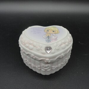 Puede incluir: Un joyero de porcelana blanca en forma de coraz&oacute;n con un relieve floral y un cristal transparente. La tapa muestra una ilustraci&oacute;n de un ni&ntilde;o rubio con las manos juntas y el texto There is Always a Place in My Heart for You.