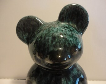 May include: A ceramic bear figurine with a green and black glaze. The bear has a simple, cartoon-like face and large ears.