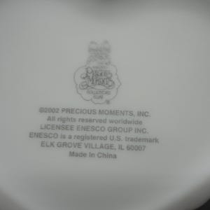 Puede incluir: Una base de cer&aacute;mica blanca con el logotipo de Precious Moments Collectors Club y el texto: 2002 PRECIOUS MOMENTS, INC. All rights reserved worldwide. LICENSEE ENESCO GROUP INC. ENESCO is a registered U.S. trademark. ELK GROVE VILLAGE, IL 60007. Made In China.