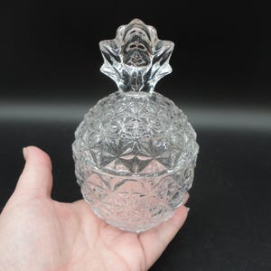Könnte beinhalten: Eine durchsichtige Glasdose in Form einer Ananas mit Deckel. Die Dose hat ein rautenförmiges Muster.
