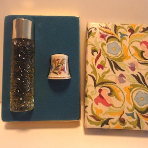 May include: An antique perfume bottle with a silver cap and a decorative glass design, a small thimble, and a floral patterned box. The thimble and box feature colorful floral designs. The items are displayed on a teal blue surface.