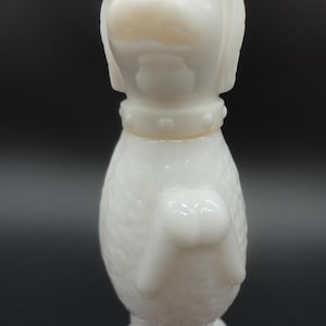 May include: A white, vintage dog figurine with a textured body and a collar with small, raised dots. The dog's head is upright, and the figurine has a glossy finish. The background is a dark gray.