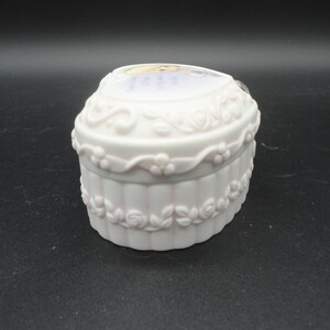Puede incluir: Un joyero de porcelana blanca en forma de coraz&oacute;n con acabado mate y detalles en relieve de rosas y enredaderas en los laterales. La tapa muestra una ilustraci&oacute;n impresa de un personaje rubio e incluye el texto, Love is the best gift.