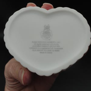 Puede incluir: Un joyero de cer&aacute;mica blanca en forma de coraz&oacute;n con un borde festoneado. La parte inferior presenta un logotipo impreso y el texto 1998 PRECIOUS MOMENTS, INC. All rights reserved worldwide. LICENSEE ENESCO GROUP INC. ENESCO is a registered U.S. trademark.