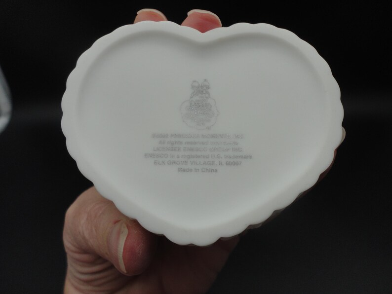 Puede incluir: Un joyero de cer&aacute;mica blanca en forma de coraz&oacute;n con un borde festoneado. La parte inferior presenta un logotipo impreso y el texto 1998 PRECIOUS MOMENTS, INC. All rights reserved worldwide. LICENSEE ENESCO GROUP INC. ENESCO is a registered U.S. trademark.