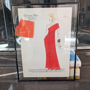 Könnte beinhalten: Gerahmte Vintage-Modeillustration eines roten One-Shoulder-Kleides von Christian Dior. Das Kunstwerk zeigt eine Skizze einer Frau in dem Kleid, mit einem roten Stoffmuster befestigt. Der Rahmen ist schwarz.