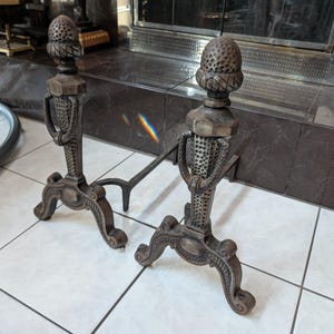 Puede incluir: Par de morillos antiguos de chimenea de hierro fundido. Los morillos tienen un acabado marrón oscuro con una parte superior en forma de bellota, una columna decorativa y patas curvas. Diseñados para sostener leños en una chimenea.
