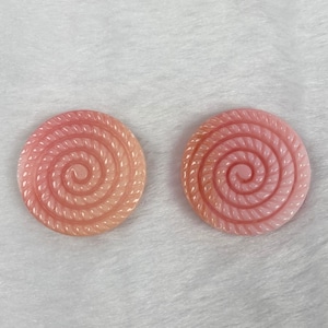 Può includere: Due bottoni rotondi rosa e bianchi con un motivo a spirale. I bottoni sono rotondi e presentano un motivo a spirale in rilievo.