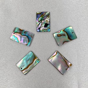 以下が含まれることがあります： 吊り下げ用の穴が上部に開いた、虹色のアワビ貝の四角いペンダントが5つ。貝殻は緑、青、紫、金など、さまざまな色をしています。