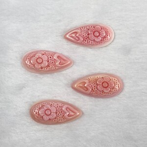 May include: Four pink shell-shaped hair clips with a floral design. Each clip has a small pink flower in the center and a heart-shaped design on either side.