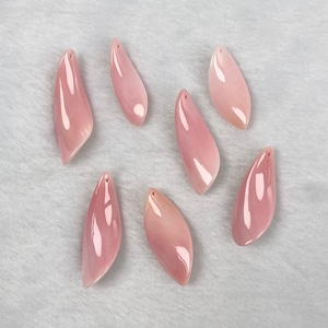 Pode incluir: Oito pingentes de concha rosa com um furo na parte superior para encordar. As conchas são lisas e têm uma forma natural e orgânica.