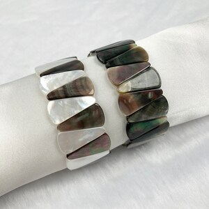 May include: Two bracelets made of black and white shell pieces. The bracelets are made of triangular shaped pieces of shell that are arranged in a pattern.