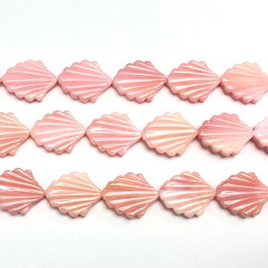 Op de afbeelding: Rijen roze schelpkralen met witte ribbels. De schelpvormige kralen hebben een glanzende afwerking. De kralen zijn geregen, klaar voor het maken van sieraden of andere knutselprojecten.