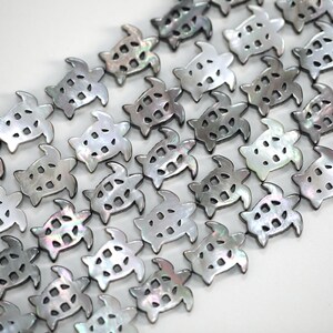 May include: Rows of iridescent, turtle-shaped beads. Each bead is a light gray color with a pearlescent sheen, and has a cut-out design. The beads are arranged diagonally across a white background, suggesting they are for jewelry making or crafts.