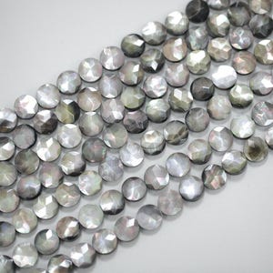 Puede incluir: Primer plano de hileras de cuentas redondas, facetadas e iridiscentes en tonos grises, plateados y negros. Las cuentas tienen un aspecto nacarado y están dispuestas en diagonal. Adecuadas para la creación de joyas.