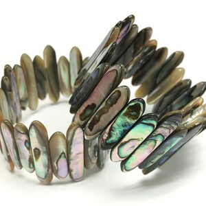 May include: Abalone shell bracelet with iridescent colors of green, purple, and brown. The bracelet is made of elongated, polished shell pieces strung together. The bracelet is shown on a white background.