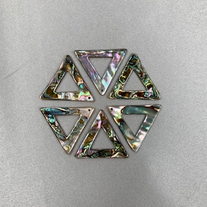 Puede incluir: Seis colgantes triangulares iridiscentes de concha de abulón. Cada triángulo tiene un agujero en la parte superior para ensartar. Las conchas muestran una gama de colores, incluyendo verde, morado y plateado. Los colgantes están dispuestos en un patrón hexagonal.