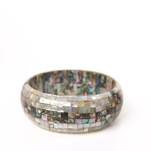 May include: A wide, mosaic-style bracelet. The bracelet is made of small, square tiles in shades of white, gray, and iridescent colors. The bracelet has a rounded shape and a smooth surface. The overall theme is jewelry.
