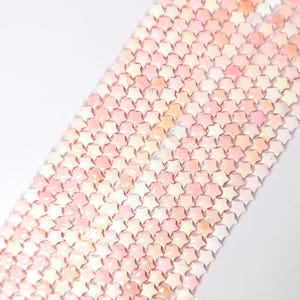 May include: Close-up of a collection of star-shaped beads in shades of pink, peach, and white. The beads are arranged closely together, creating a textured surface. The beads are likely for jewelry making or crafting.